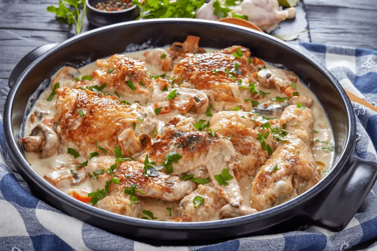 Golden-browned chicken fricassee in a creamy sauce garnished with parsley, served in a round black dish.