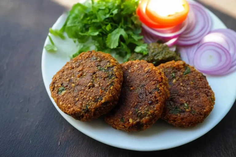 A plate of vegetarian shami kebabs: golden-brown patties garnished with sliced onions, tomatoes, coriander, and served with green chutney.